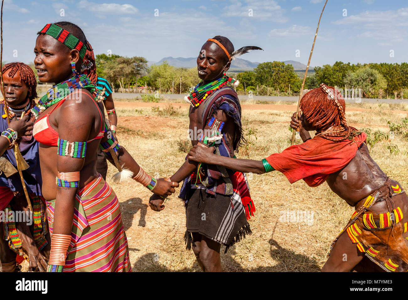 Giovani donne Hamar Taunt A Hamar Tribesman alla fustigazione essi durante un 'proveniente dall'età' Bull Jumping cerimonia, Dimeka, Valle dell'Omo, Etiopia Foto Stock