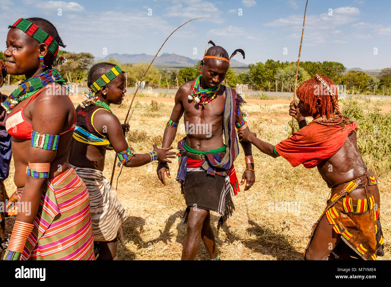 Giovani donne Hamar Taunt A Hamar Tribesman alla fustigazione essi durante un 'proveniente dall'età' Bull Jumping cerimonia, Dimeka, Valle dell'Omo, Etiopia Foto Stock
