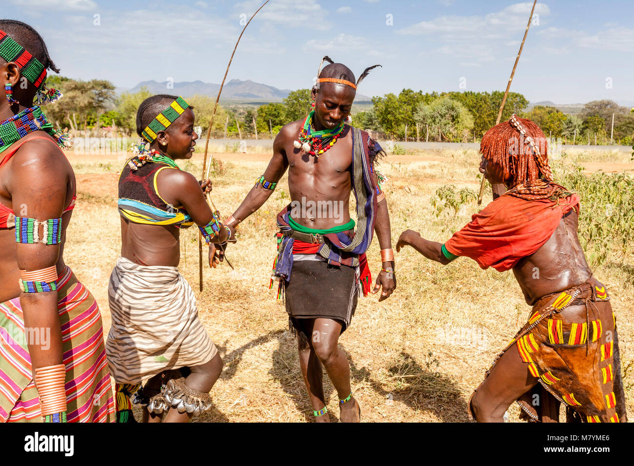 Giovani donne Hamar Taunt A Hamar Tribesman alla fustigazione essi durante un 'proveniente dall'età' Bull Jumping cerimonia, Dimeka, Valle dell'Omo, Etiopia Foto Stock