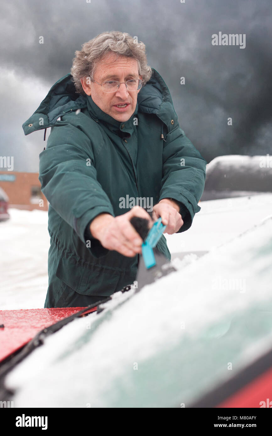 Uomo determinato la raschiatura della neve e del ghiaccio al di fuori del parabrezza della sua vettura midwinter nel Vermont Foto Stock