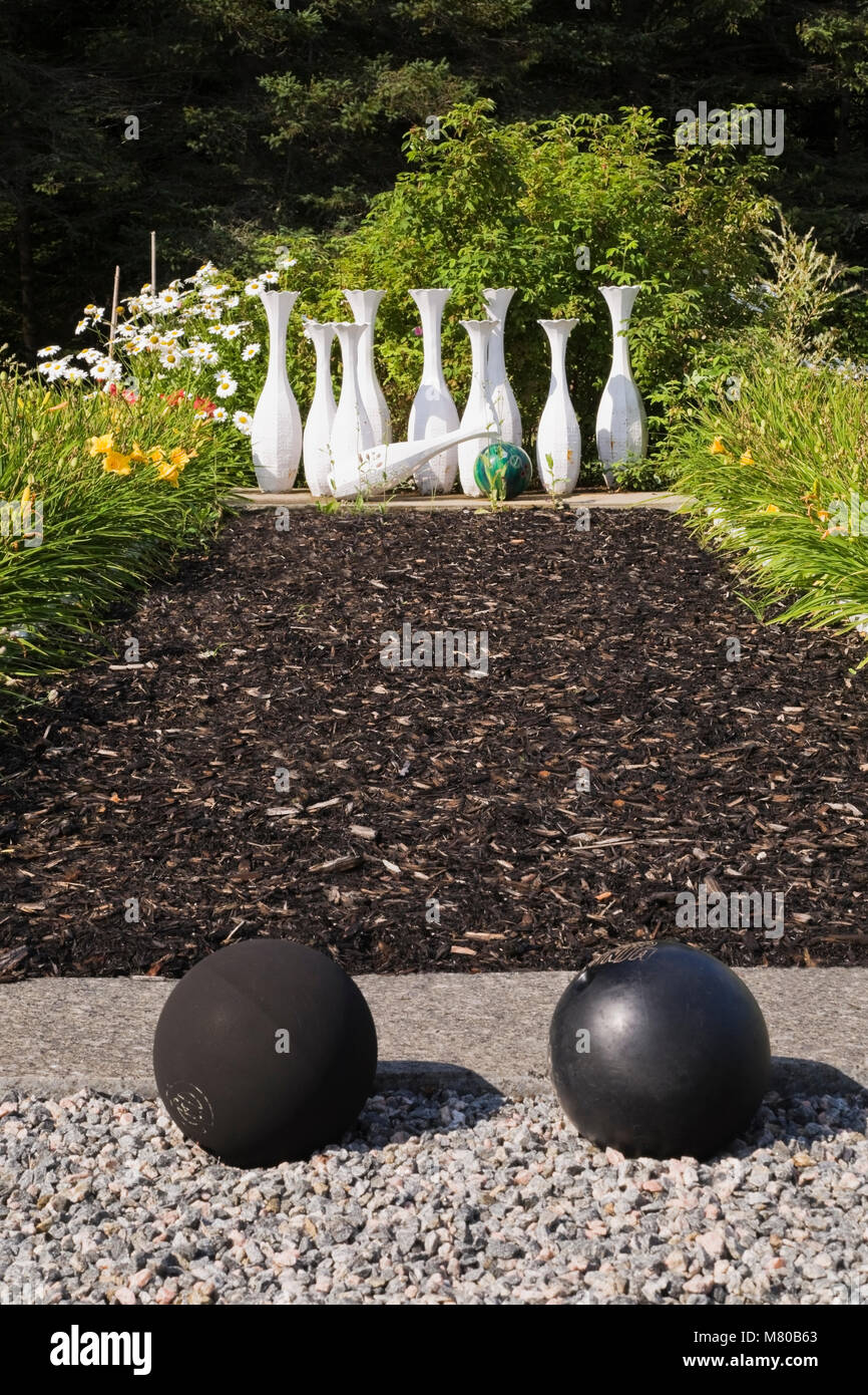 Il nero le palle da bowling e strame alley con calcestruzzo bowling perni in un paesaggistico cortile residenziale giardino d'estate. Foto Stock