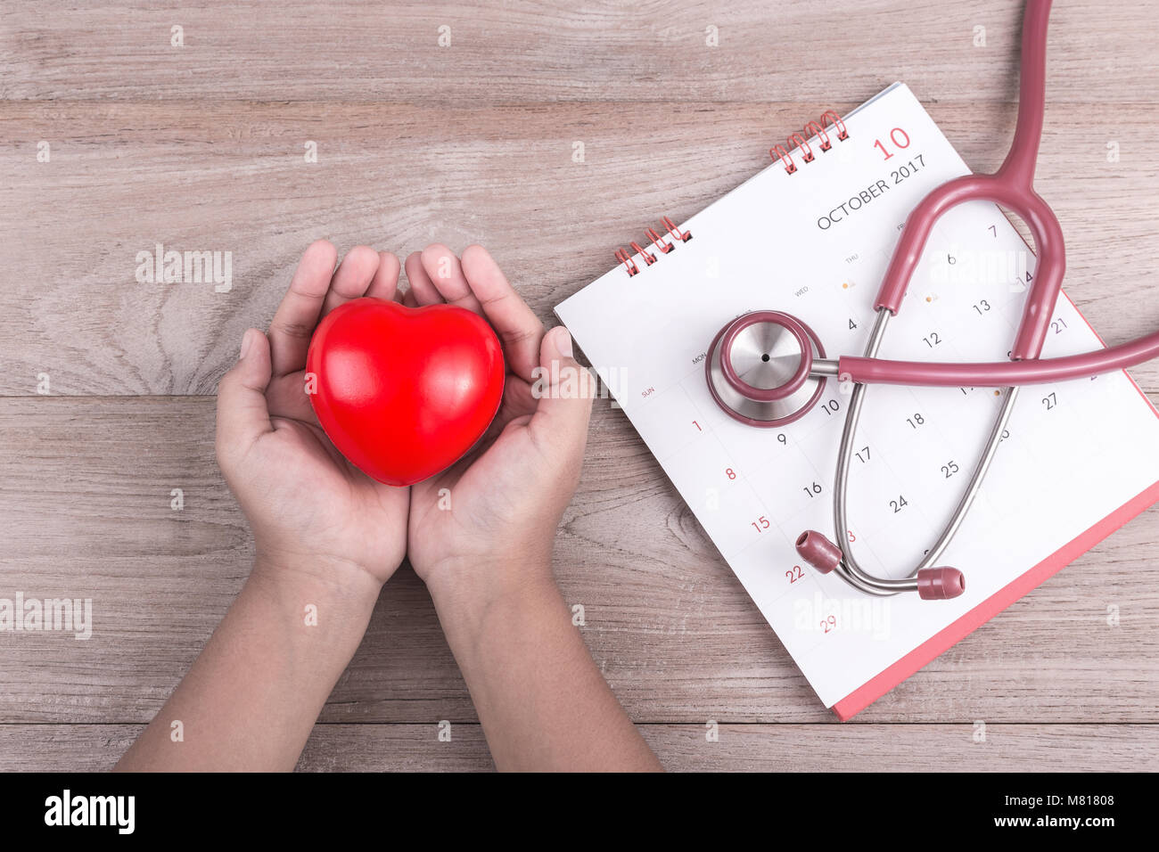 Controllare il concetto di cuore : Donna mani cuore rosso e uno stetoscopio in legno marrone sfondo tabella Foto Stock