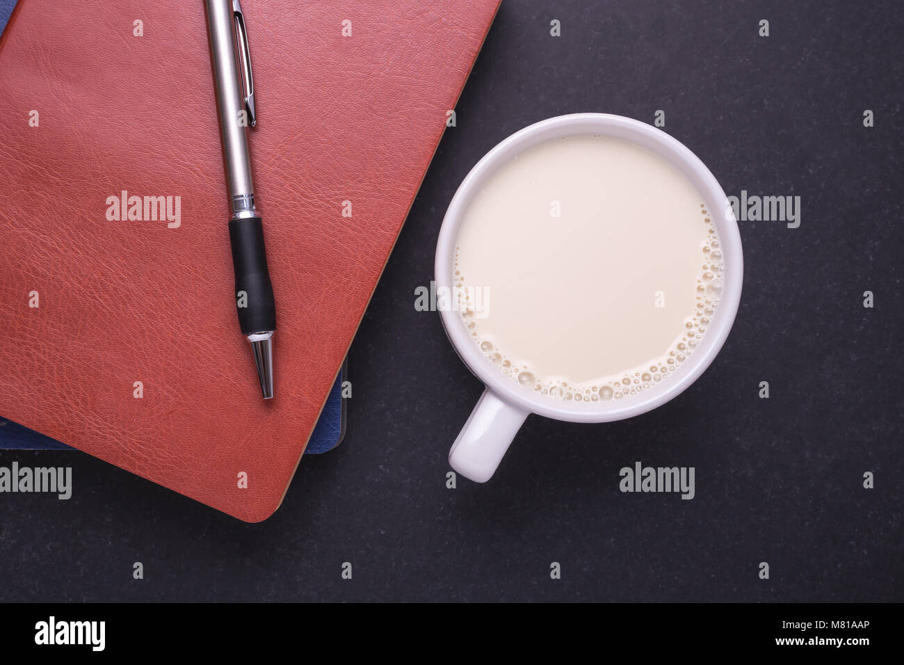 Latte in vetro bianco e nota libro sulla pietra nera di sfondo della tabella. Vista superiore e Studio shot Foto Stock