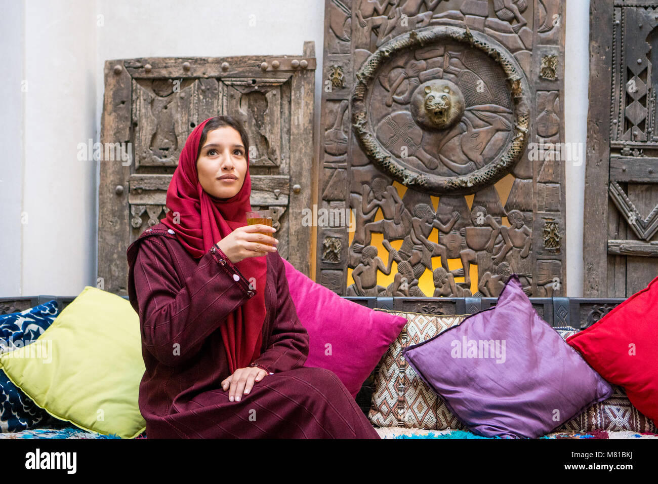 Donna musulmana di bere un tè tradizionale in rosso con abbigliamento hijab sul suo capo nel tradizionale medio ambiente orientale Foto Stock