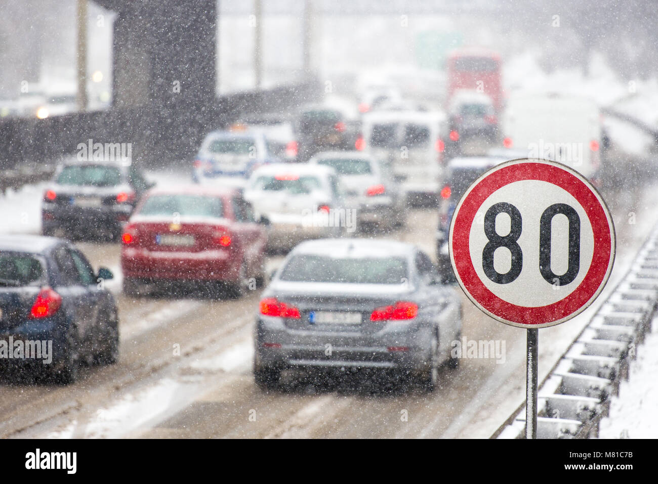 In inverno il traffico durante la tempesta di neve con scarsa visibilità. Segnale di limite di velocità con un traffico in background su una strada sdrucciolevole coperto con sn Foto Stock
