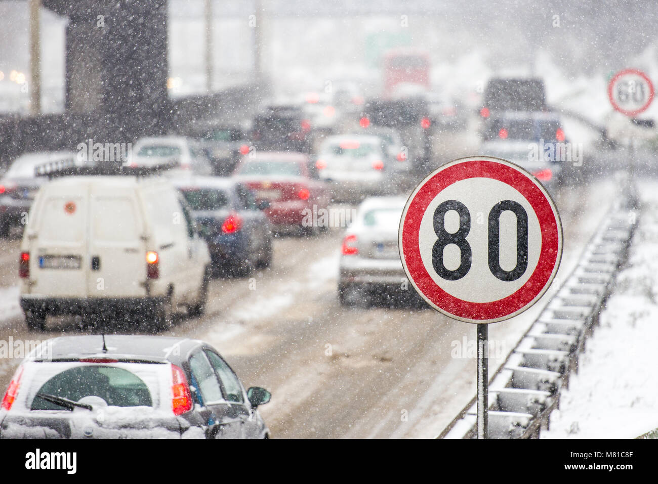 In inverno il traffico durante la tempesta di neve con scarsa visibilità. Segnale di limite di velocità con un traffico in background su una strada sdrucciolevole coperto con sn Foto Stock