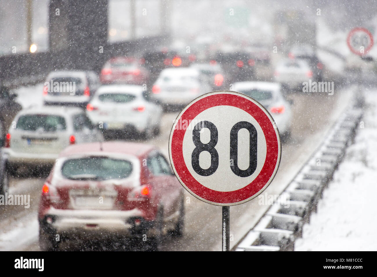In inverno il traffico durante la tempesta di neve con scarsa visibilità. Segnale di limite di velocità con un traffico in background su una strada sdrucciolevole coperto con sn Foto Stock