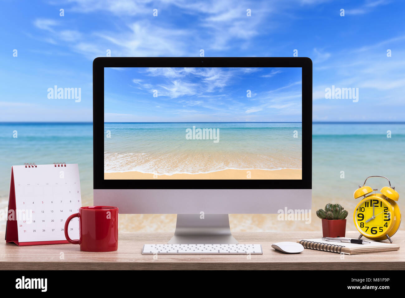 Moderno computer desktop, tazza di caffè, Sveglia, notebook e calendario sul tavolo di legno e la vista della spiaggia tropicale sfondo. Salvate con il ritaglio di pat Foto Stock