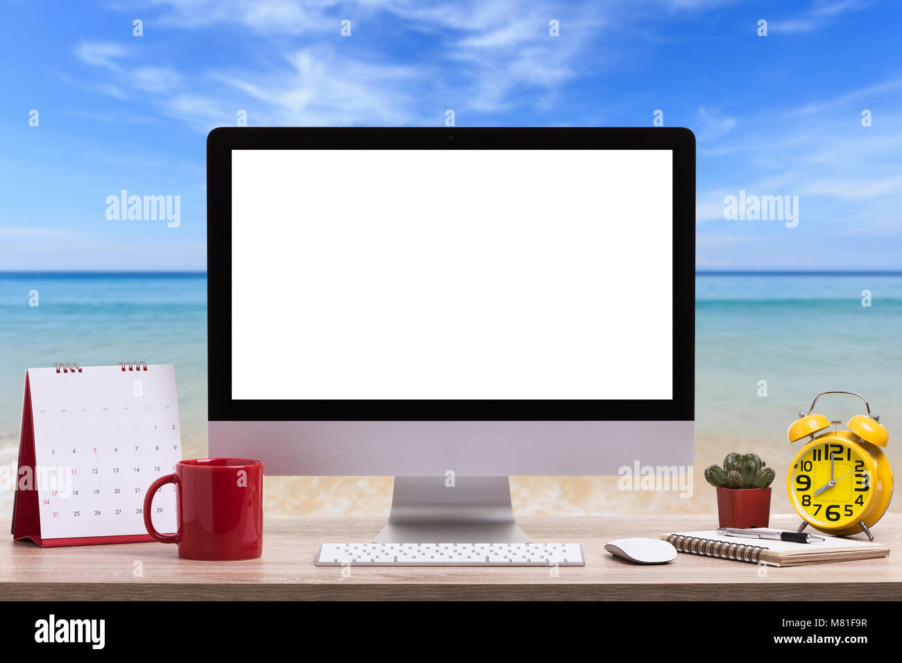 Moderno computer desktop, tazza di caffè, Sveglia, notebook e calendario sul tavolo di legno e la vista della spiaggia tropicale sfondo. Salvate con il ritaglio di pat Foto Stock