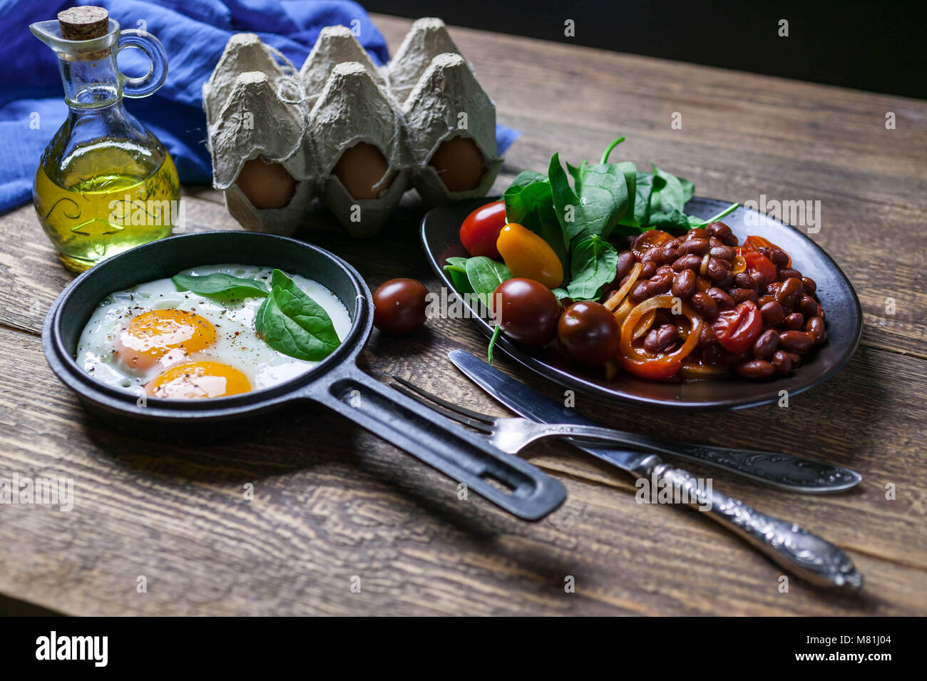 Il pan uova fritte, fagioli bianchi stufati in salsa di pomodoro e spinaci freschi. Concetto di una sana prima colazione. Foto Stock