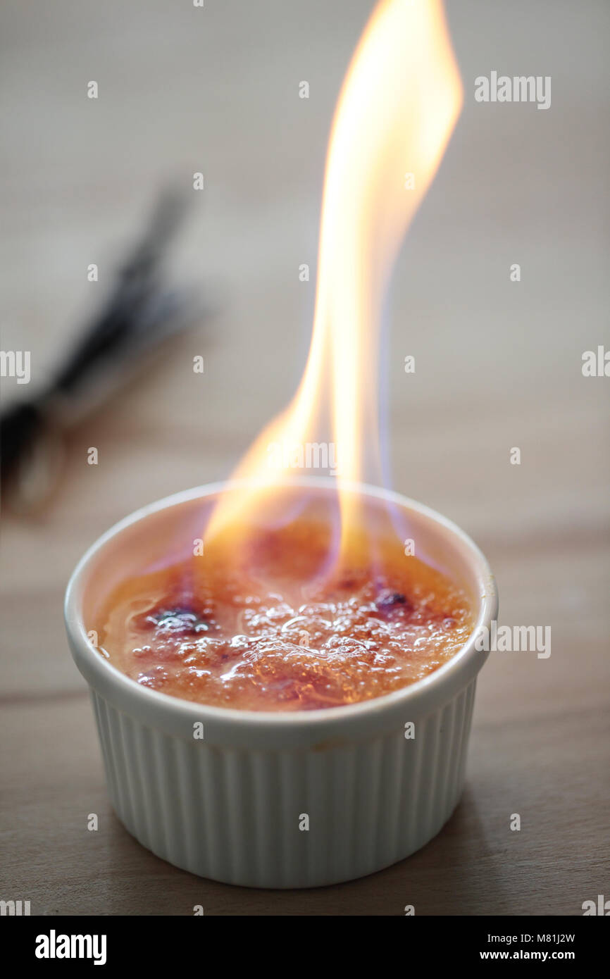 La masterizzazione di alcool sulla parte superiore delle creme brulee dessert Foto Stock
