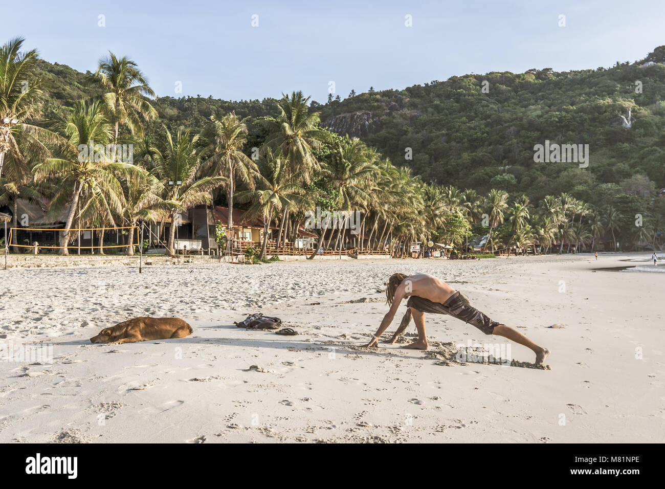 La mattina presto allenamento sulla luna piena festa sulla spiaggia. Giovane uomo che si allunga dopo aver dormito sulla spiaggia, Haad Rin, Koh Pangan, Thailandia, 6 maggio 2016, Foto Stock