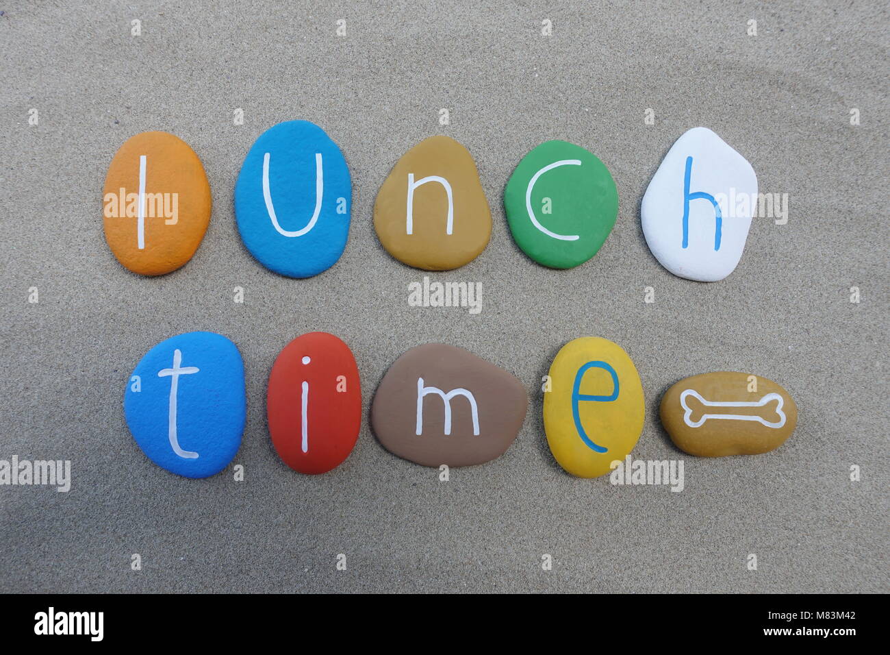 Ora di pranzo, concettuale pietre multicolore composizione sulla spiaggia di sabbia Foto Stock