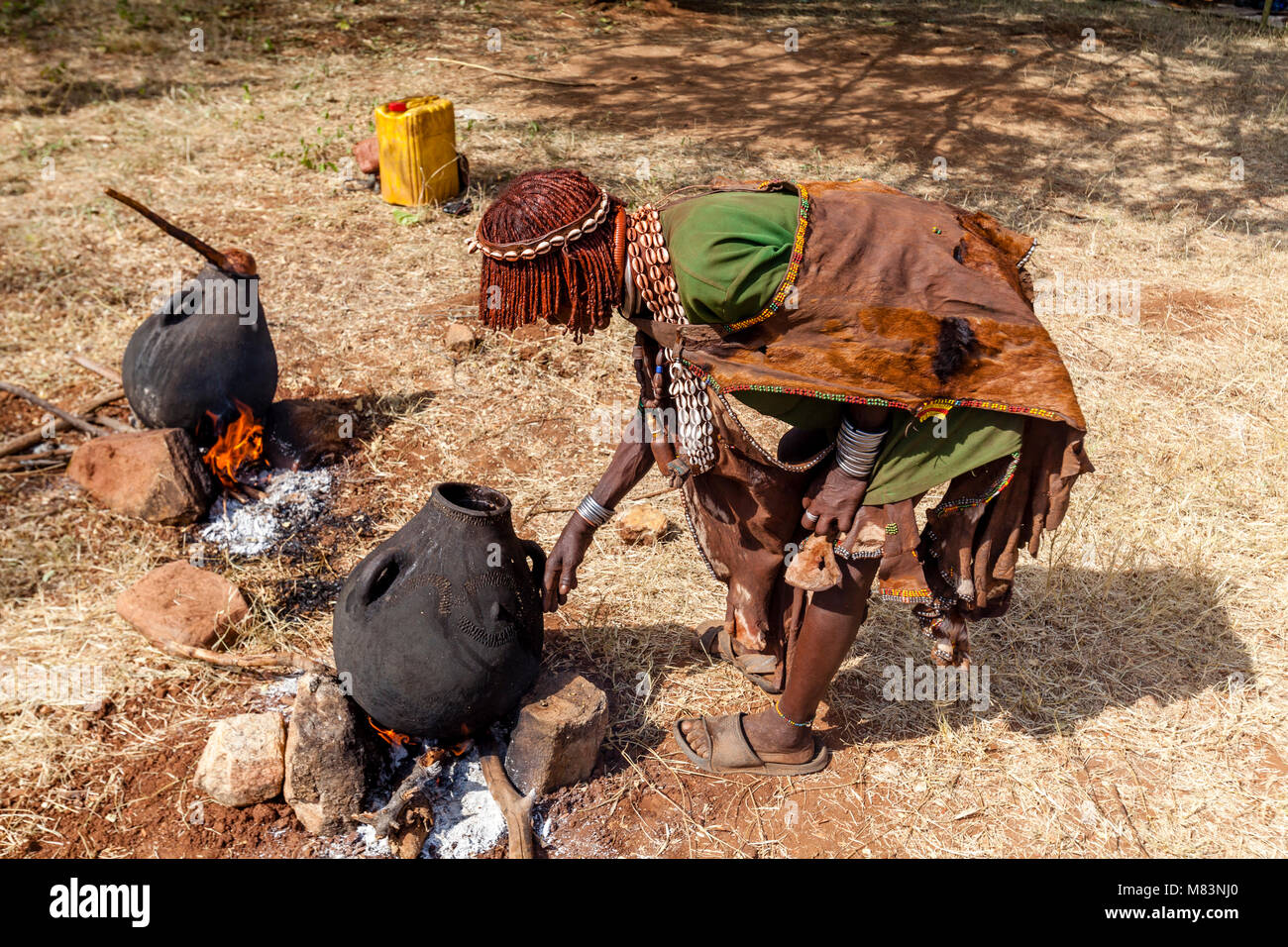 Un Hamar donna per la cottura sul fuoco aperto a Hamar villaggio vicino Dimeka, Valle dell'Omo, Etiopia Foto Stock