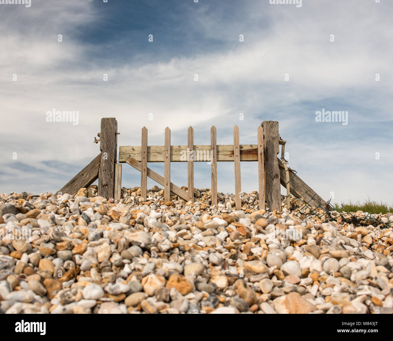 Il cancello seppellì nella spiaggia di ciottoli andando da nessuna parte con lo sfondo del cielo. Foto Stock
