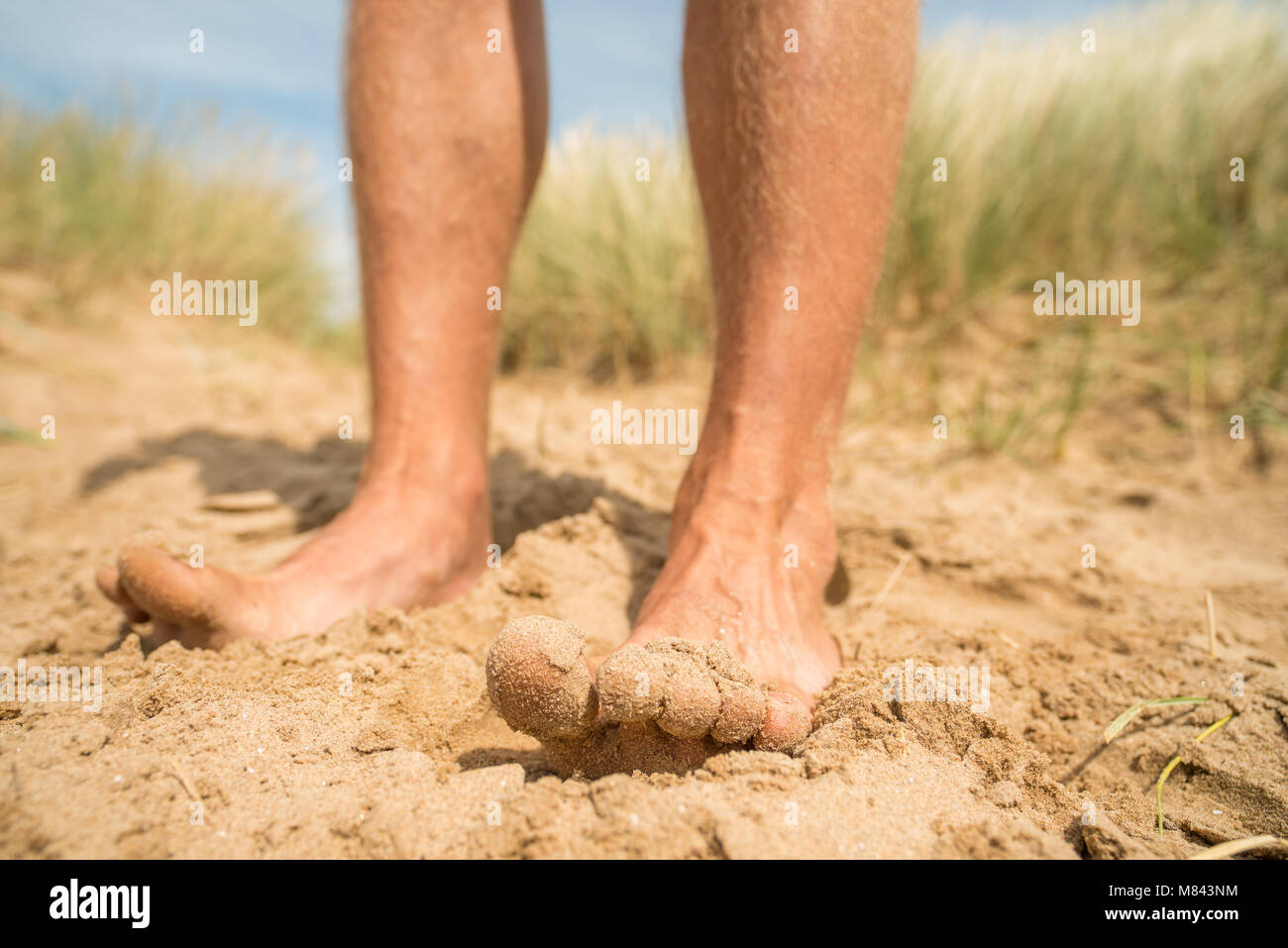 Maschio di gambe e piedi in piedi su una spiaggia di sabbia godendo la sensazione Foto Stock
