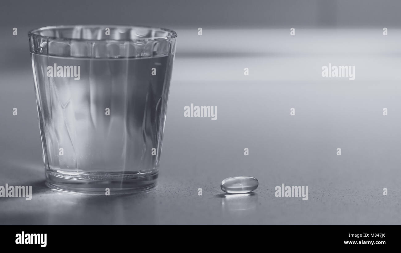 Vitamina capsule con un bicchiere di acqua sul tavolo Foto Stock