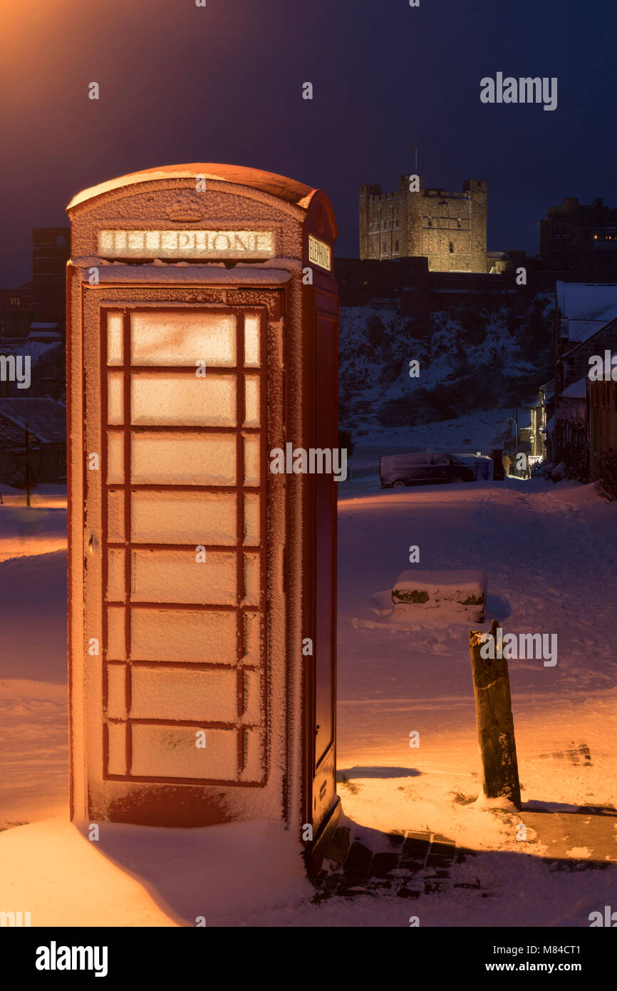 Tradizionale in rosso casella telefono e il castello di Bamburgh in inverno la neve, Northumberland, Inghilterra. Inverno (febbraio) 2018. Foto Stock