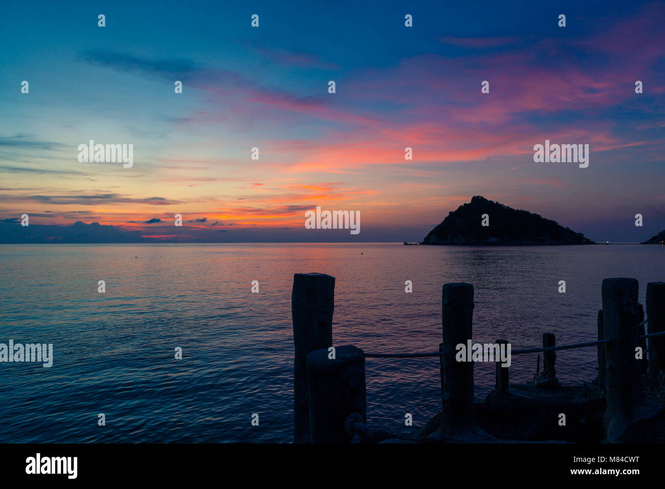 Incredibile tramonto sul mare, affacciato su Isola Nang Yuan da Ko Tao, bastoni di legno di un molo in primo piano e una rosa giallo arancio e blu cielo Foto Stock