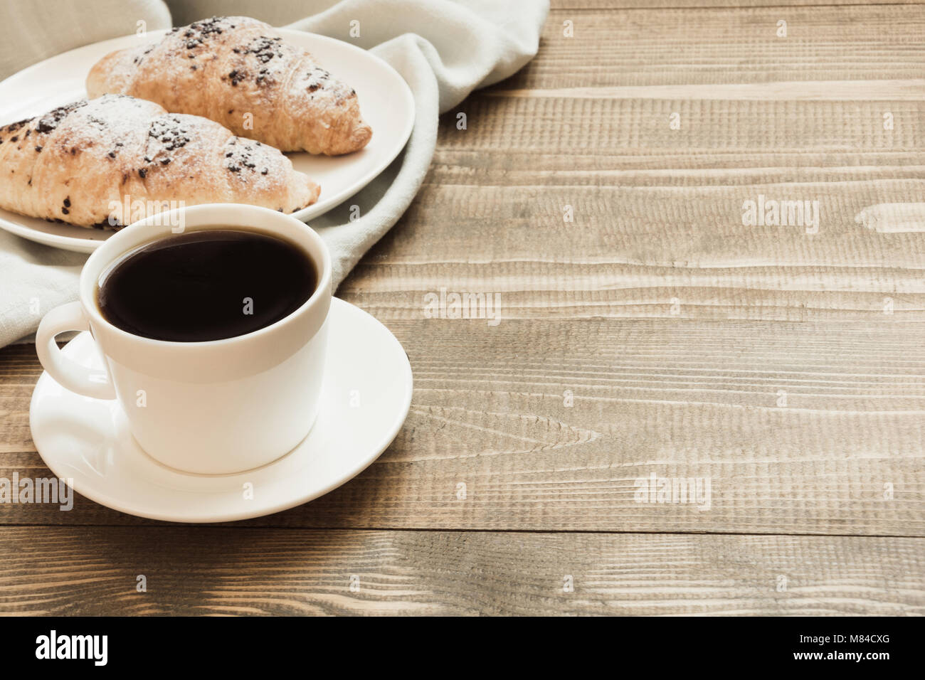 Pane appena sfornato croissant al cioccolato e la tazza di caffè nero sul tagliere di legno. Close up. Concetto di colazione. Copia dello spazio. Foto Stock