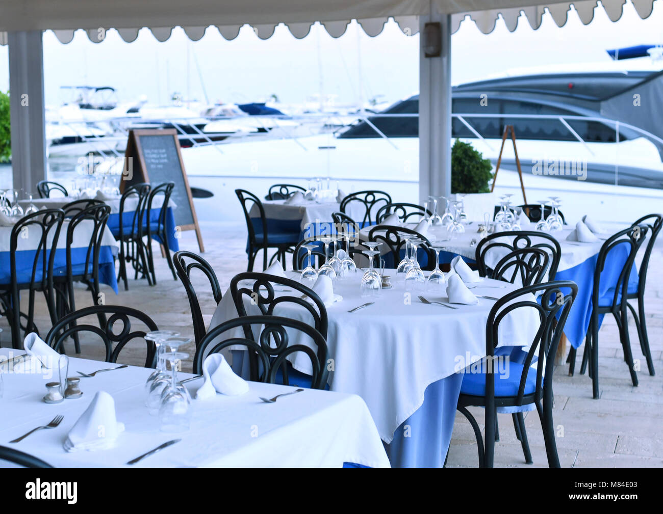 Il ristorante del porto con sedi vuote e impostazione tabella. cena tabelle ad un porto di yacht, ancorato con barche e navi. Foto Stock