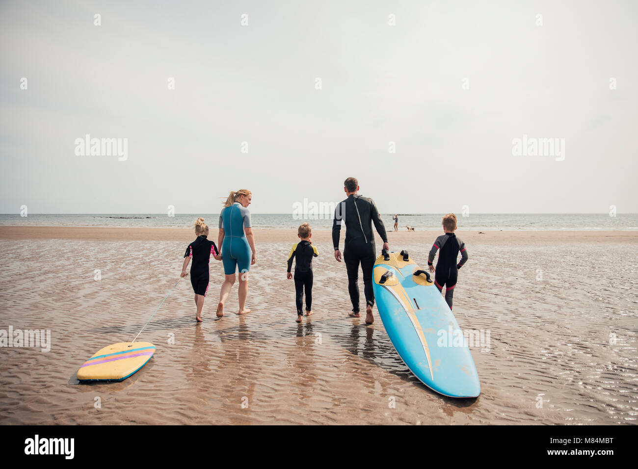 Famiglia a piedi al bordo delle acque per surfing. Foto Stock