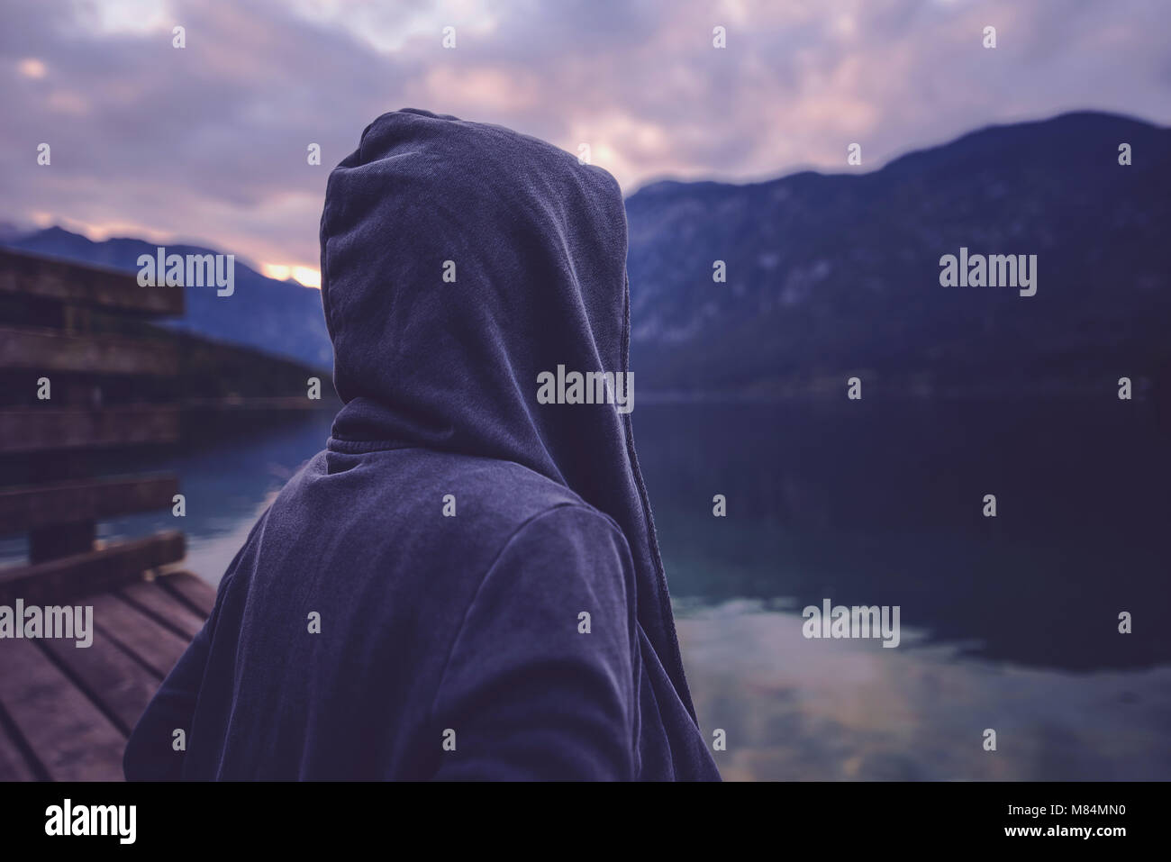 Lonely incappucciati persona di sesso femminile in piedi vicino al lago e guardando la montagna bella e paesaggio forestale nel tramonto, ultra violet tonica ombre Foto Stock