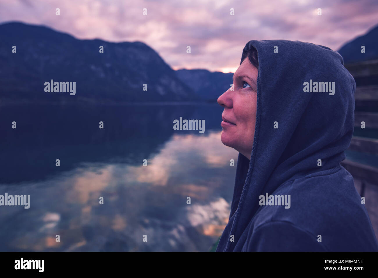 Lonely donna guardando il cielo drammatico. Persona di sesso femminile in felpa con cappuccio in piedi da solo dal lago, ultra violet tonica ombre Foto Stock