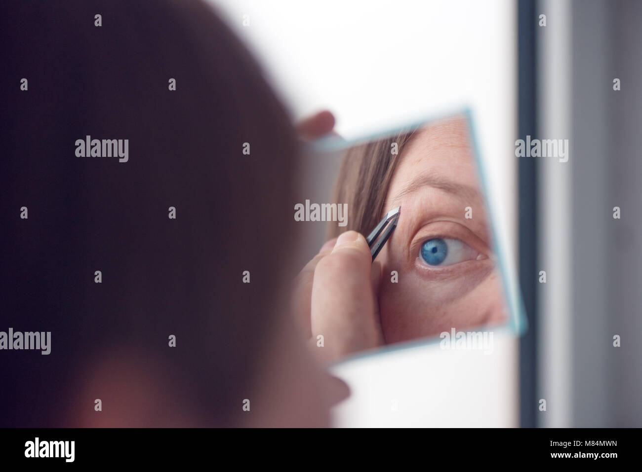 Donna spiumatura sopracciglia con pinzette dalla finestra, il fuoco selettivo Foto Stock