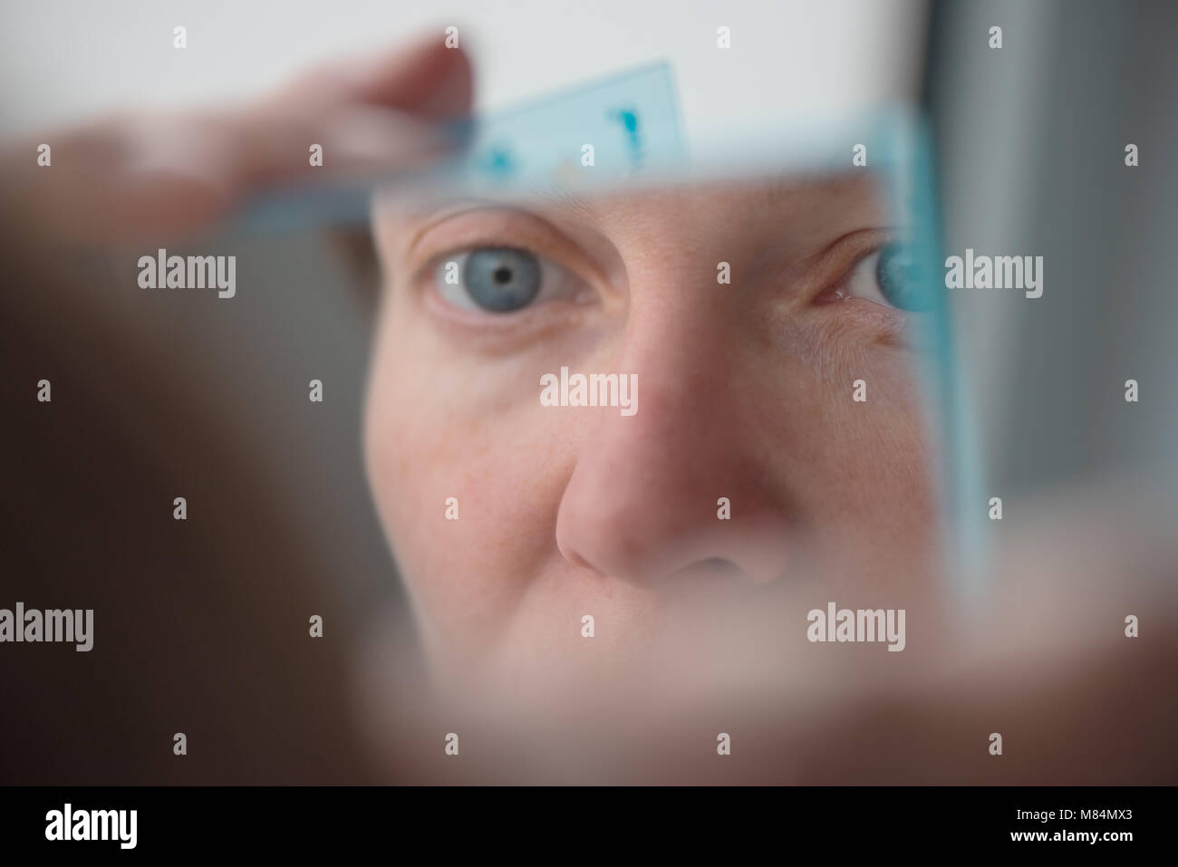 Donna spiumatura sopracciglia con pinzette dalla finestra, il fuoco selettivo Foto Stock