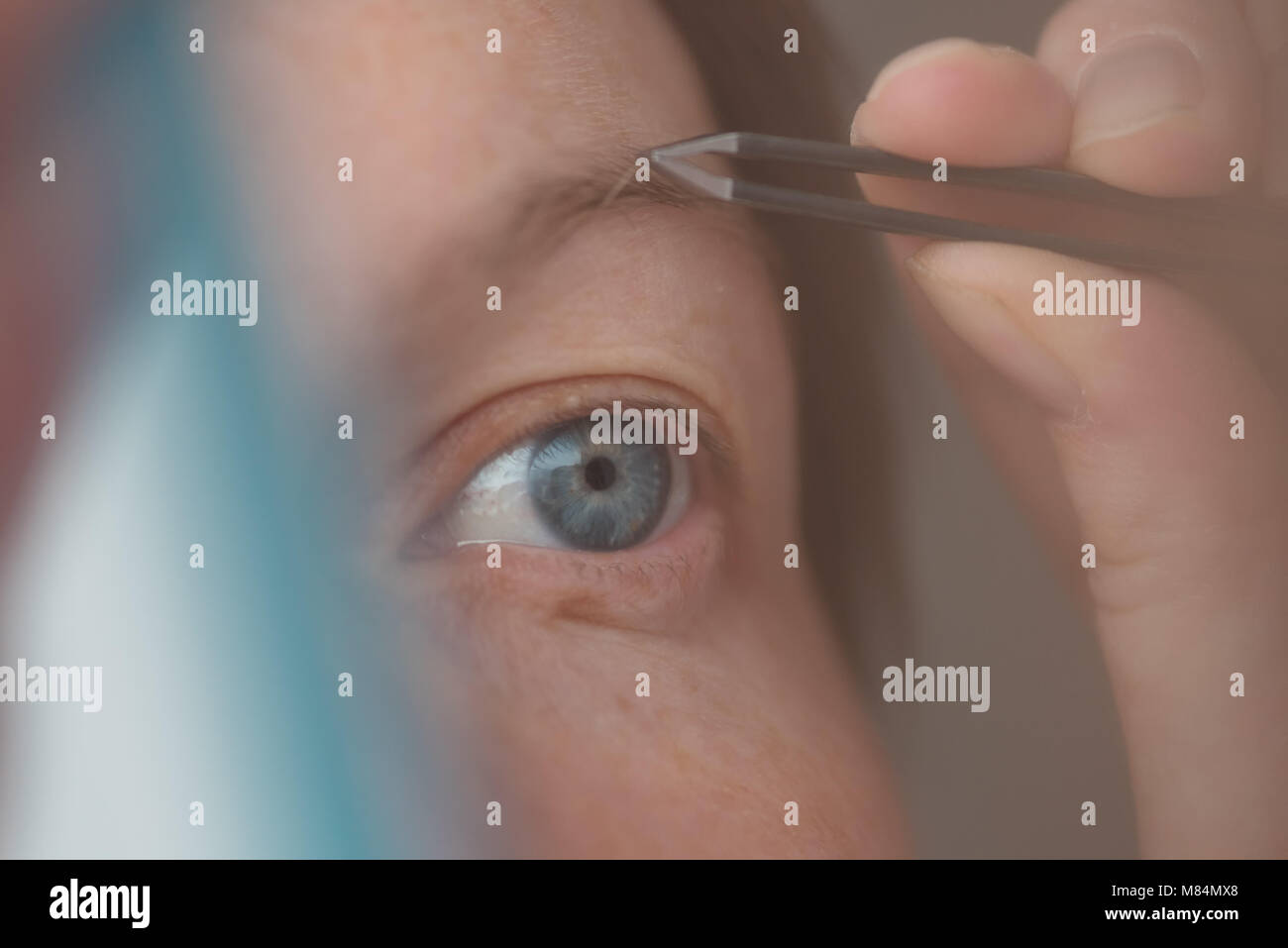 Donna spiumatura sopracciglia con pinzette dalla finestra, il fuoco selettivo Foto Stock