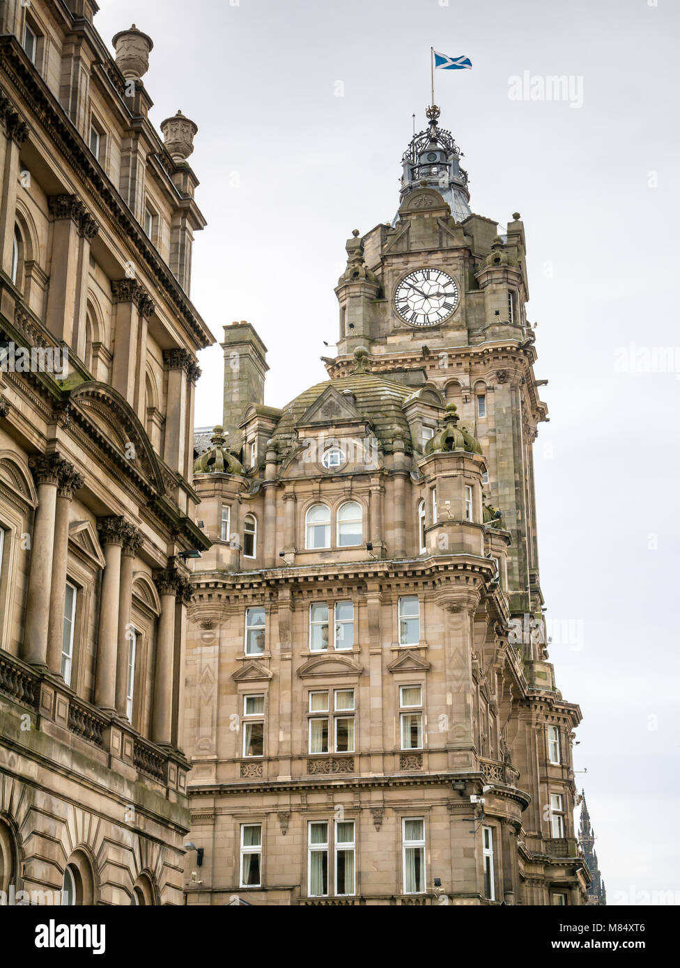Guardando il Vittoriano ornati Balmoral Hotel clock tower, Princes Street, Edimburgo, Scozia, con si intraversa battenti bandiera Foto Stock