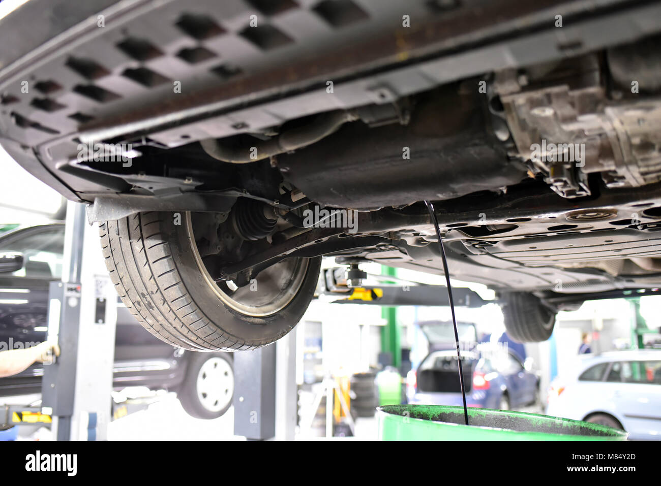 Cambio dell'olio motore in un garage - il veicolo sulla piattaforma di sollevamento - scarico di olio usato Foto Stock Cambio dell'olio motore in un garage - il veicolo sulla piattaforma di sollevamento - scarico di olio usato Foto Stock