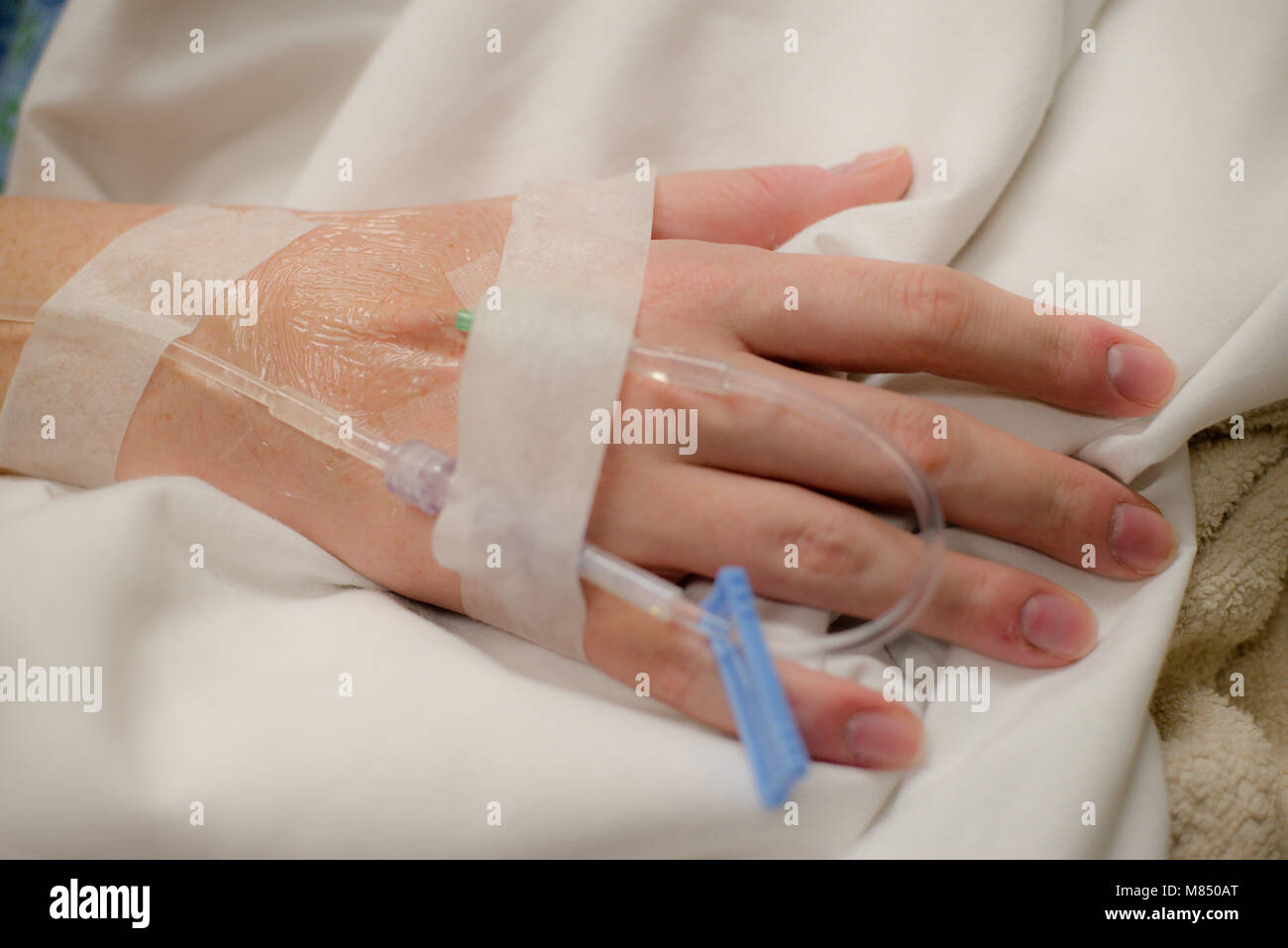 L'immagine orizzontale di mano con fluido intravenious nastrato poggiante su coltre bianca in ospedale. Terapia intravenosa Foto Stock