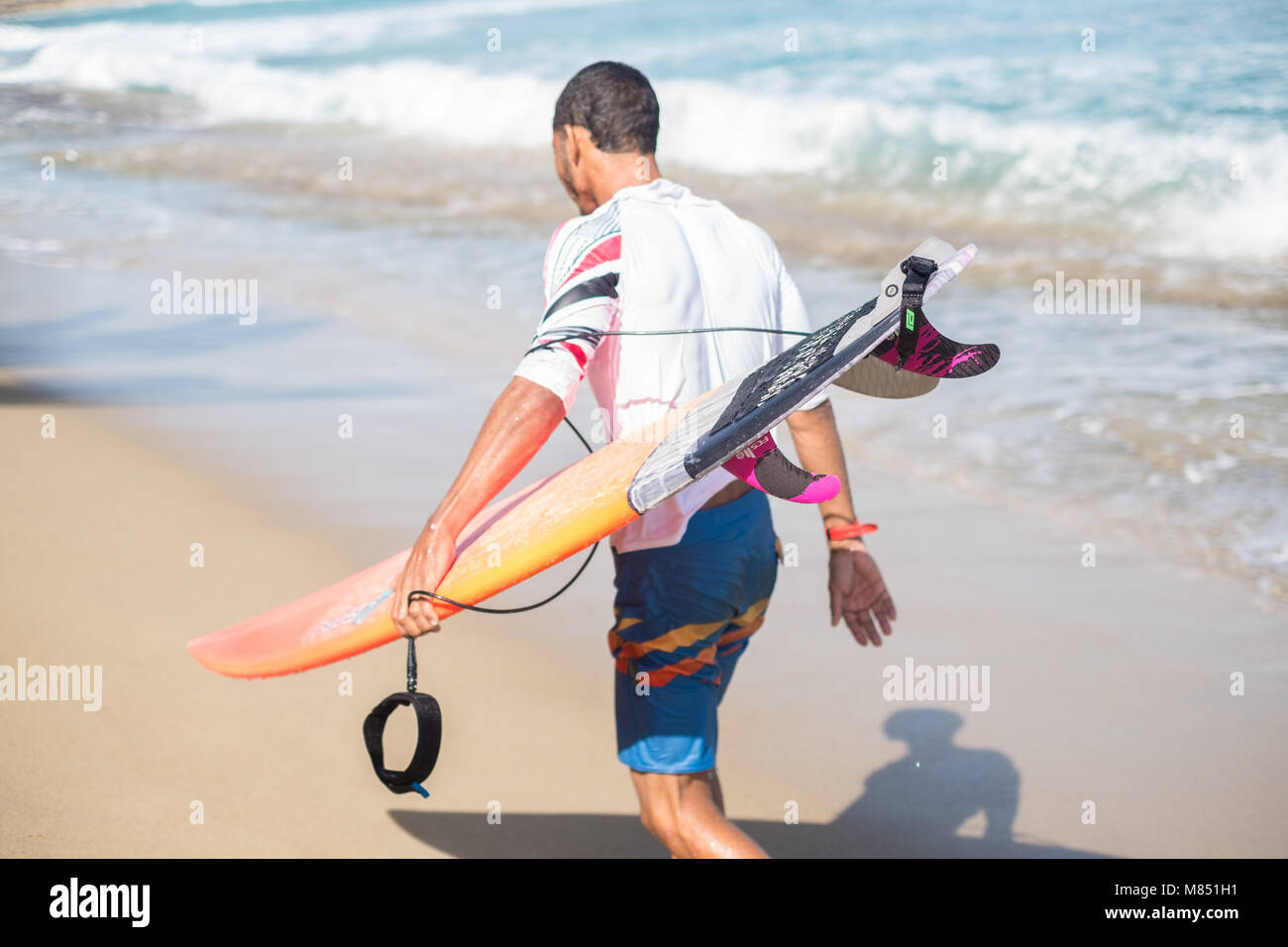 Un surfista passeggiate su una spiaggia tropicale. Foto Stock