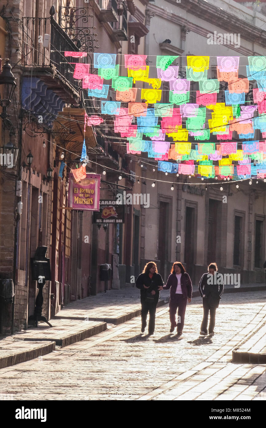 I messicani camminando sulla strada di ciottoli con sun lit banner colorati Bandiere appeso sopra Foto Stock