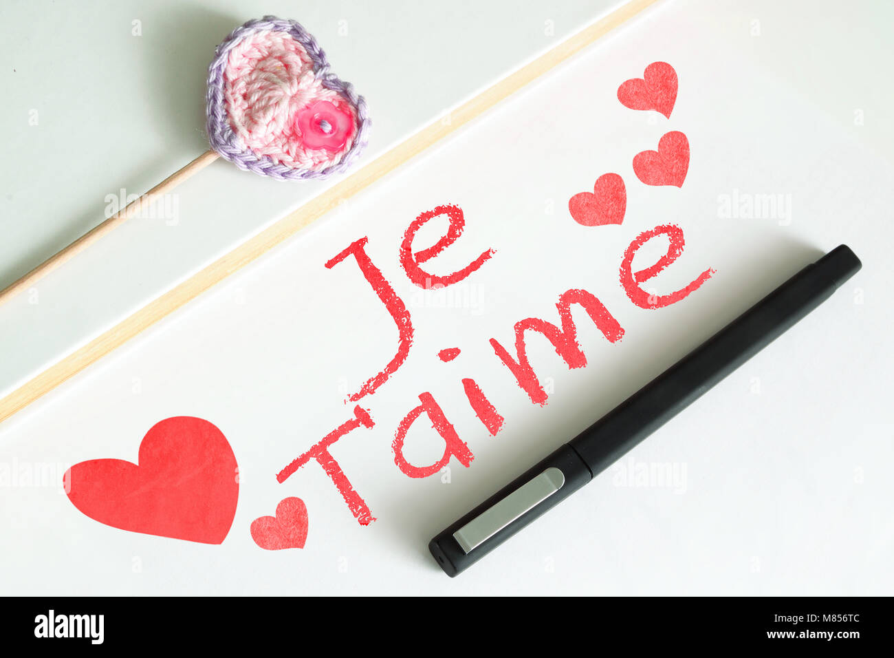Blocco note su un computer desktop in un ambiente di lavoro con il testo je t'aime (ti amo) in spagnolo. Alcuni tipi di carta, una penna e un cuore amigurumi. Foto Stock