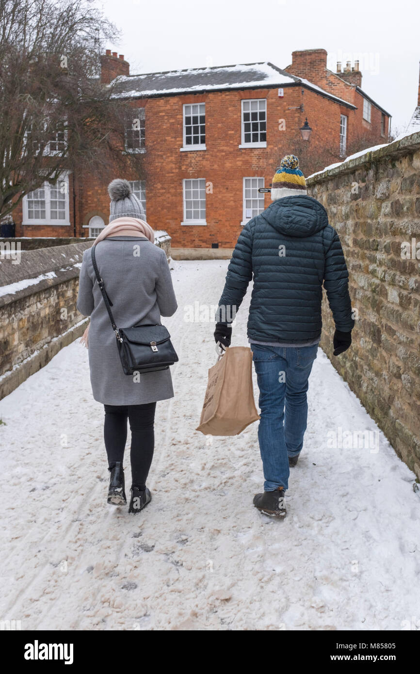 L uomo e la donna a piedi lungo un sentiero coperto di neve e ghiaccio l'uomo sta portando una borsa da shopping, sia indossando lanosi pom pom bobble cappelli Foto Stock