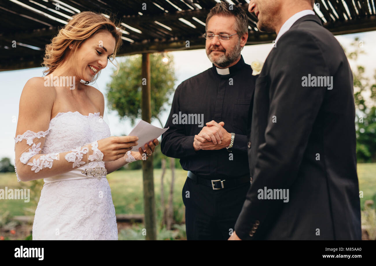 Donna di leggere i voti da carta per suo marito alla cerimonia di matrimonio dello sfondo. Partner di sesso femminile la lettura di matrimonio i voti nella cerimonia con sacerdote da. Foto Stock