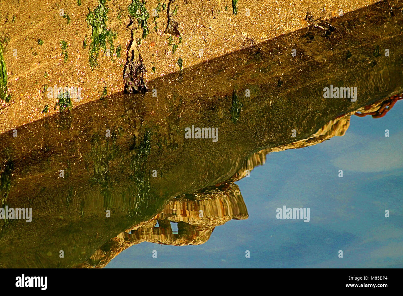 Riflessioni di un imbarcadero costiere parete in una calma piatta in mare in un porto locale. Foto Stock