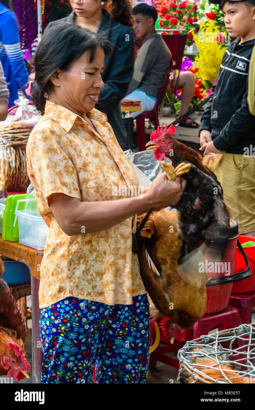 Un cliente ha un aspetto un po' worred come lei si mantiene un chcken dalle gambe e che solleva la sua testa verso di lei in un mercato all'aperto in Hoi An, Vietnam. Foto Stock