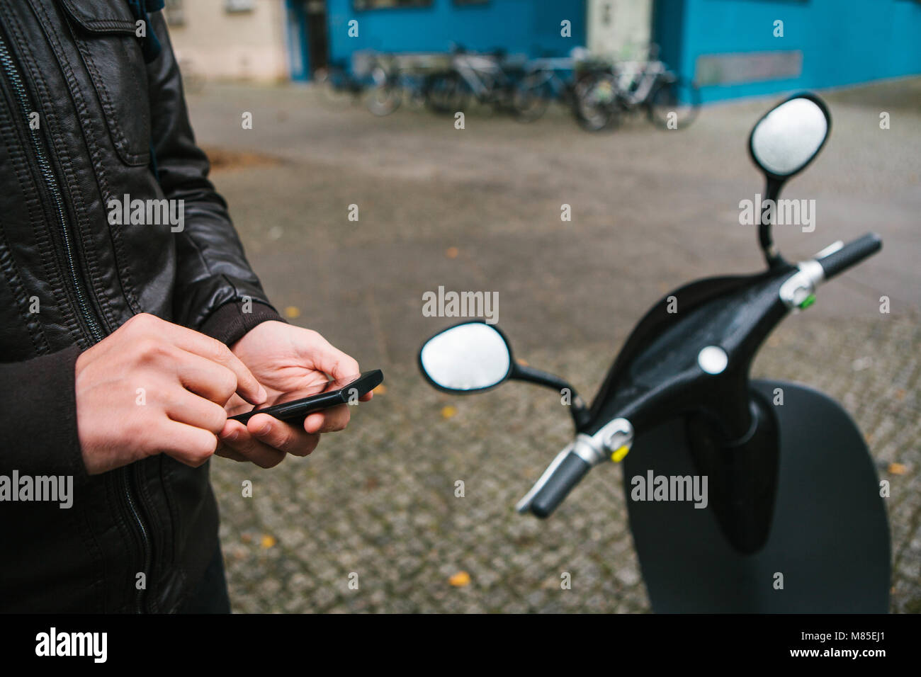 Il turista sta per usare il scooter elettrico attraverso l'applicazione mobile nel telefono e distalmente attivarlo. Un veicolo popolare di Berlino e Foto Stock