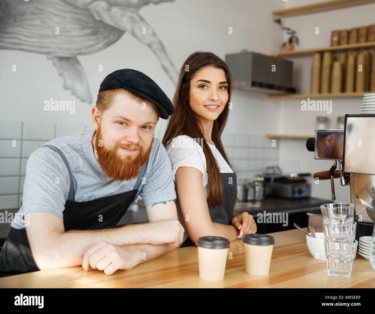 Caffè il concetto di Business - Positivo giovane uomo barbuto e bella attraente dama barista giovane nel grembiule guardando la fotocamera mentre in piedi al bancone bar Foto Stock