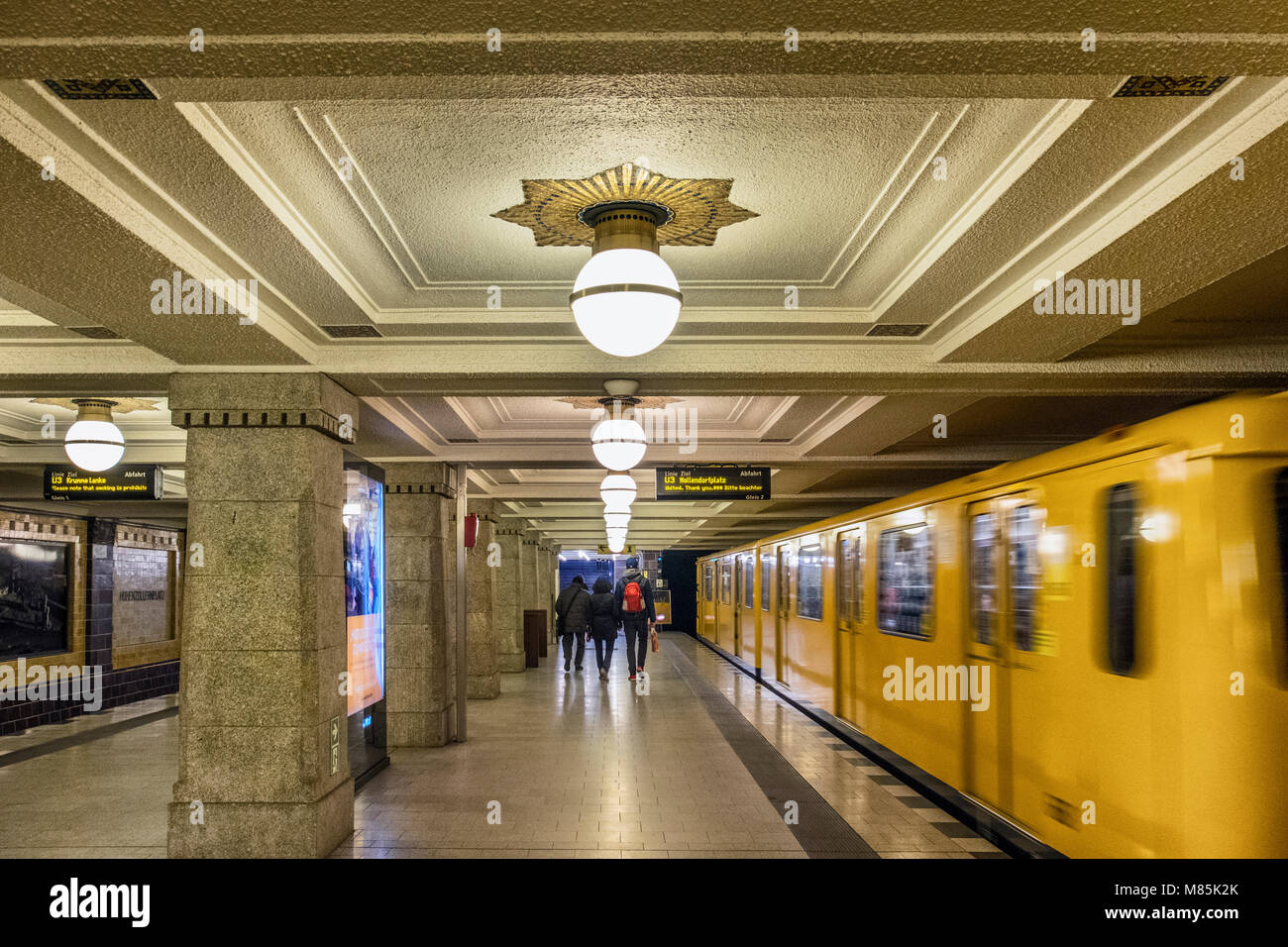 Berlino quartiere Wilmersdorf,Hohenhollernplatz U3 U-Bahn metropolitana stazione ferroviaria interna. Treno di giallo e la gente a piedi sulla piattaforma Foto Stock