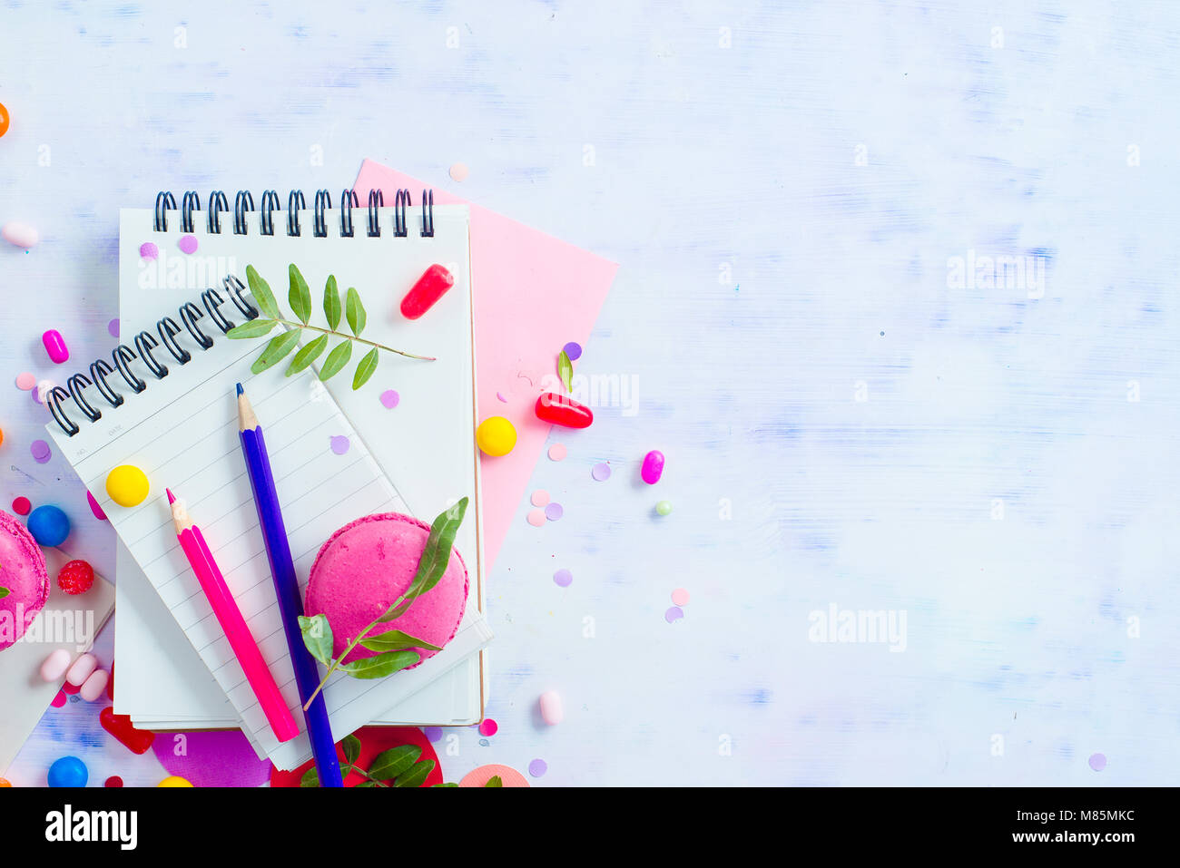 Rivestito in bianco quaderni con matite colorate, dolci e rosa macaron cookie su uno sfondo luminoso con copia spazio. Pianificazione del partito concetto di divertimento. Foto Stock