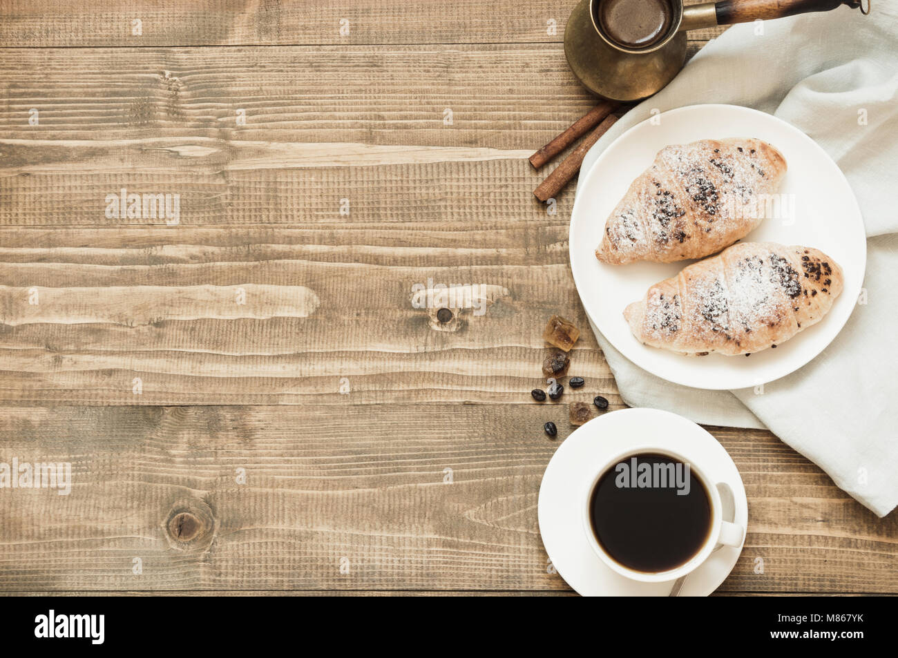 Pane appena sfornato croissant al cioccolato e la tazza di caffè nero sul tagliere di legno. Vista dall'alto. Concetto di colazione. Copia dello spazio. Foto Stock