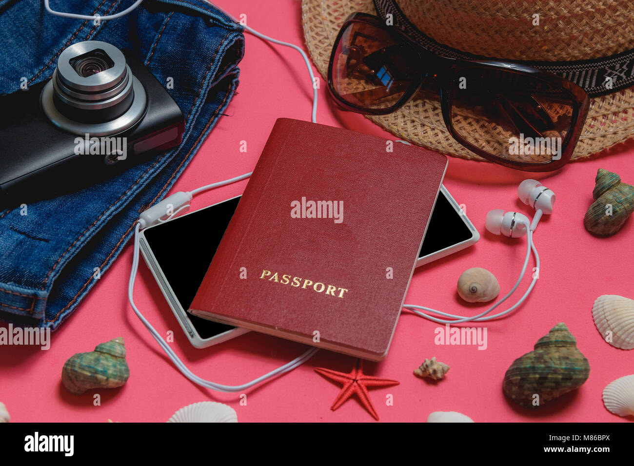 Passaporto, Smartphone, vestiti, occhiali da sole, Fotocamera, marrone cappello, su sfondo rosa. Concetto di viaggio. Foto Stock