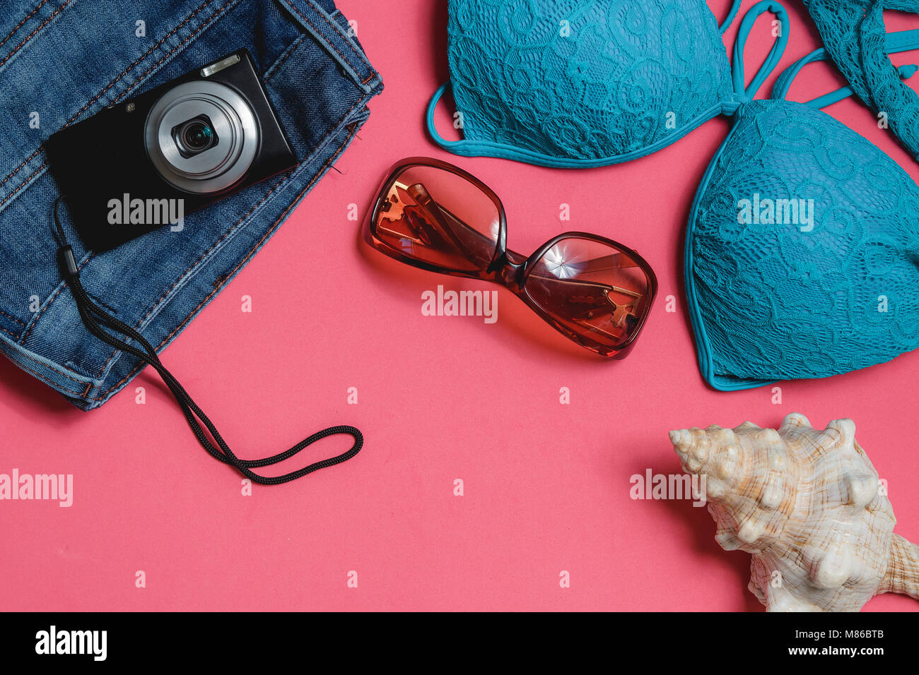 Costume da bagno, Jeans, occhiali da sole, fotocamera, il Seashell su sfondo rosa. Vista dall'alto concetto di viaggio con Copyspace. Foto Stock