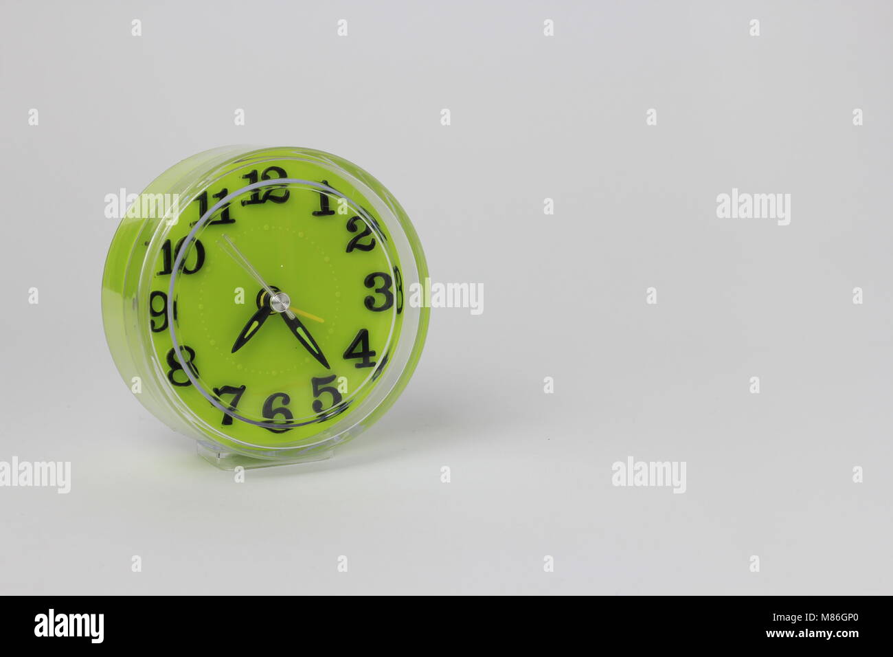 Un verde orologio sveglia con uno sfondo bianco posizionato a sinistra Foto Stock