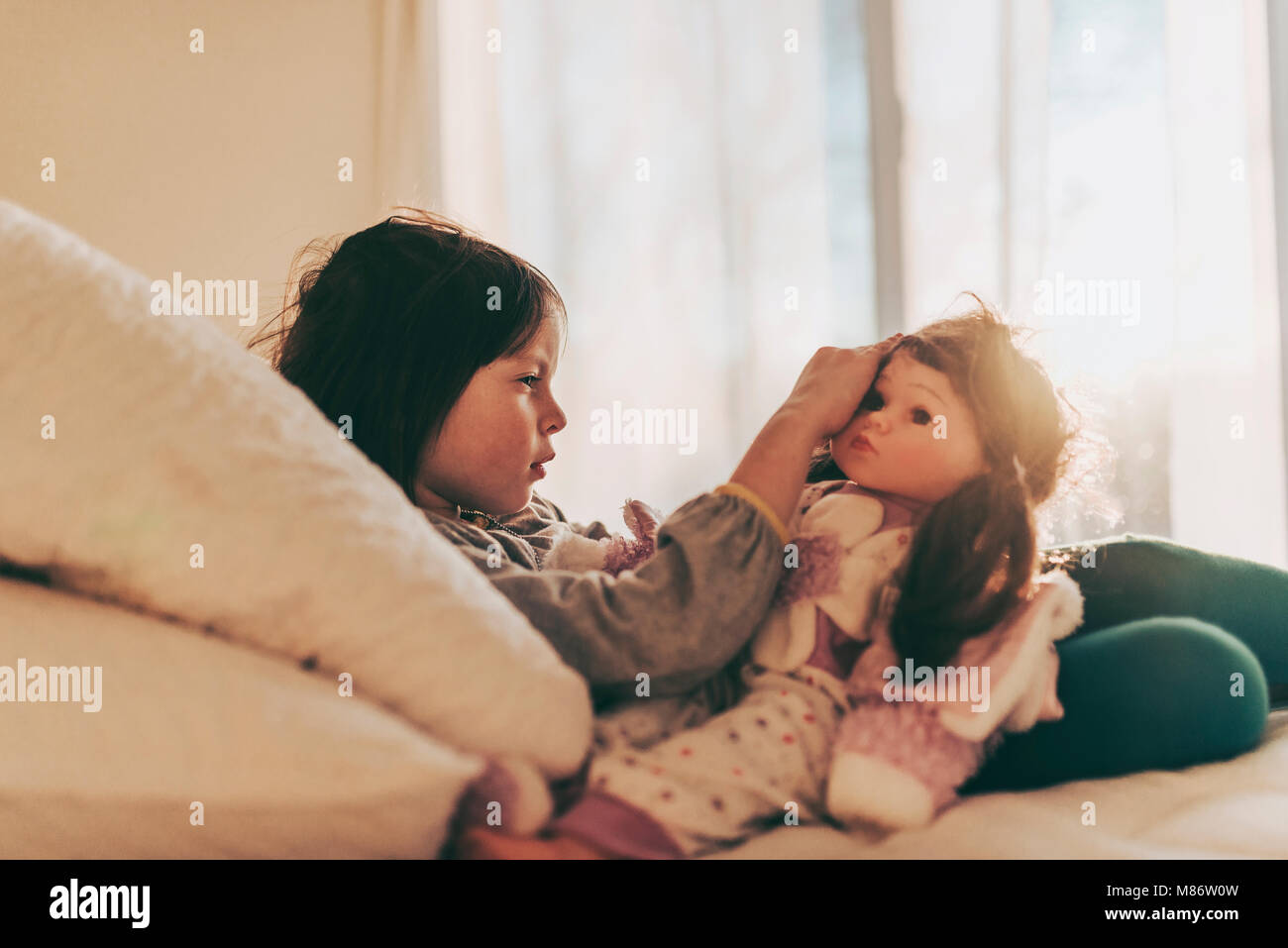 Ragazza seduta sul suo letto a giocare con una bambola Foto Stock